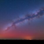 A starry night sky with the Milky Way and a red horizon glow