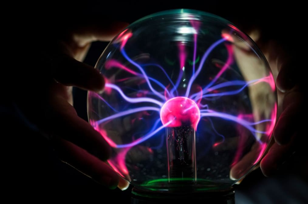 Plasma globe with pink and blue streams of electricity responding to a touching hand